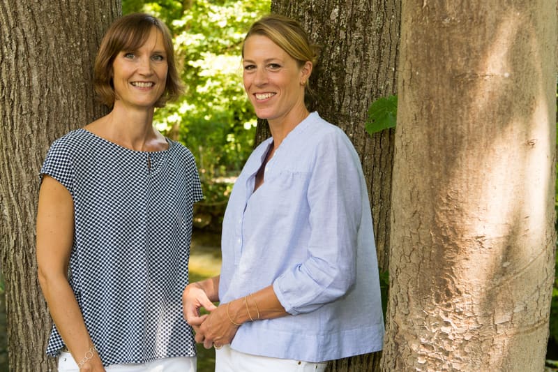 Petra Bruch (links) und Anja Wiehl (rechts) lächelnd zwischen zwei Bäumen an der Würm